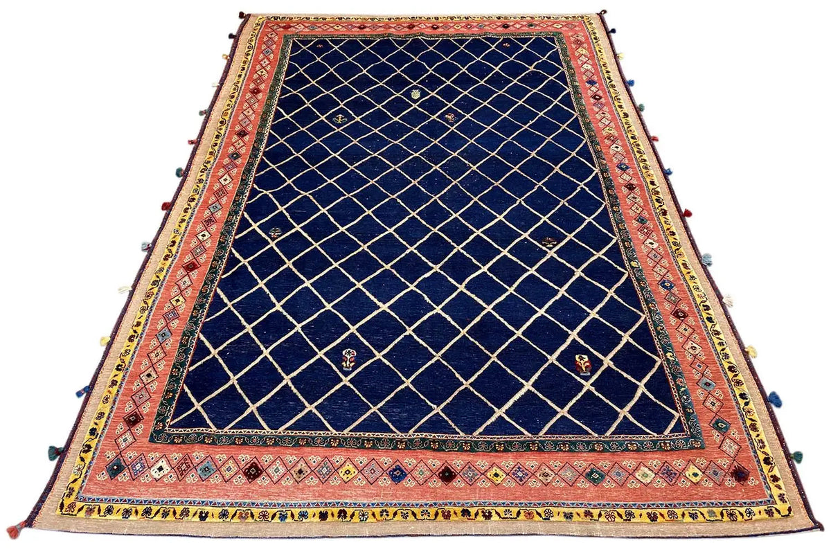 Large rug with a dark blue grid pattern, red border, and colorful tassels