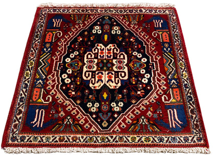 Rug with a red border, dark blue center, multicolored ornaments, and fringe